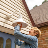 White outdoor lighting by Post & Porch, home of curb appeal accessories for the front porch and beyond; pictured is a woman installing the outdoor lighting fixture