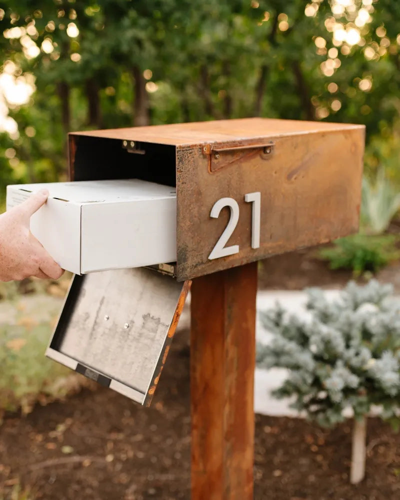 A hand placing a package into The Malone in Corten Steel, fully patinaed, house number 21