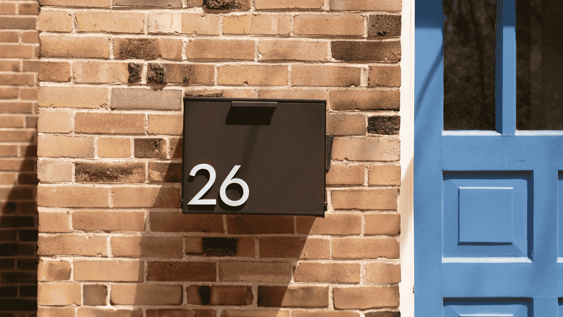 A black wall-mounted mailbox next to a blue front door by Post & Porch