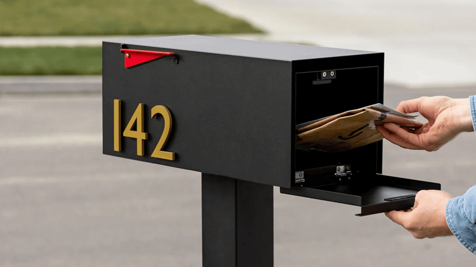 Black rear-access mailbox with gold address numbers '142' on a street, person retrieving mail.