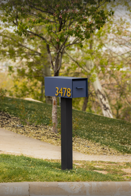 Blue rear-access mailbox and post with gold address numbers on a black post in a suburban setting.